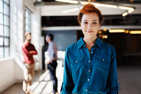 Portrait of a young businesswoman standing in an office with her colleagues in the backgroundの写真素材
