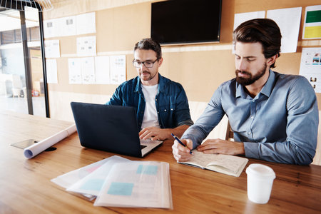 Cropped shot of two designers working on a laptop in their office