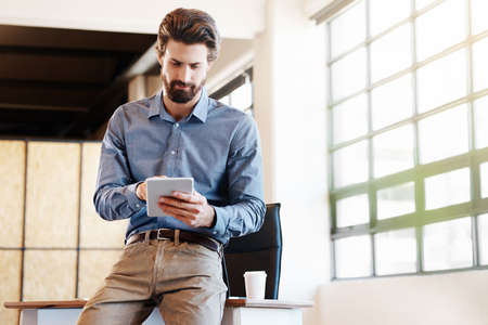 Shot of a young businessman working on his tablet in the officeの写真素材