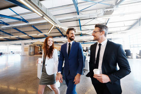 Shot of a group of colleagues walking and talking during a coffee break at workの写真素材