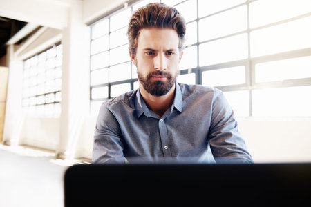 Shot of a young businessman working on his laptop in the office