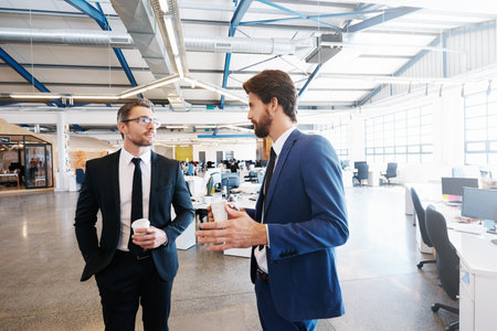 Shot of two colleagues walking and talking during a coffee break at work