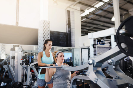 Shot of a young woman exercising at the gym with her personal trainer