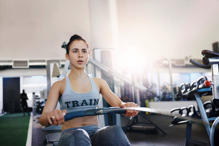 Shot of a young woman working out with a rowing machine in the gym