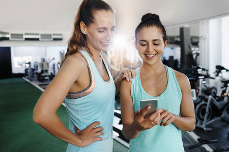 Shot of two young women using a cellphone at the gym
