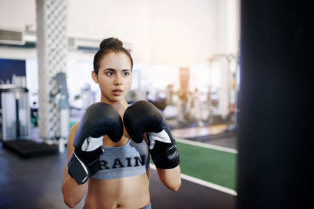 Shot of a young female boxer working out with a punching bag in the gymの写真素材