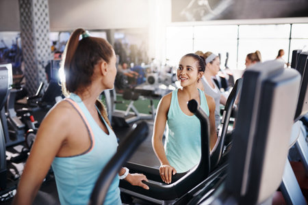 Shot of two women talking while exercising on treadmills in a gym