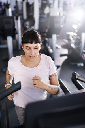 Shot of a young woman exercising on a treadmill in a gym