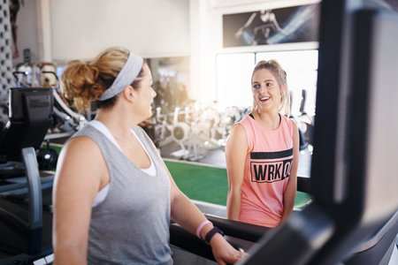Shot of two women talking while exercising on treadmills in a gymの写真素材