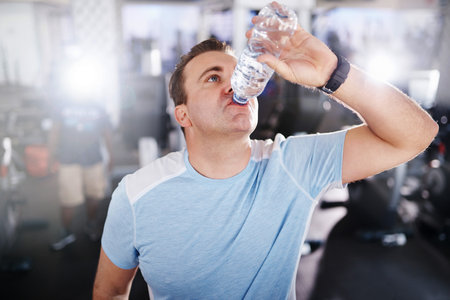 Shot of a mature man drinking water while exercising in a gymの写真素材