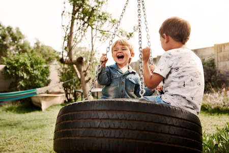 Shot of two adorable little boys playing on a swing together outdoorsの写真素材