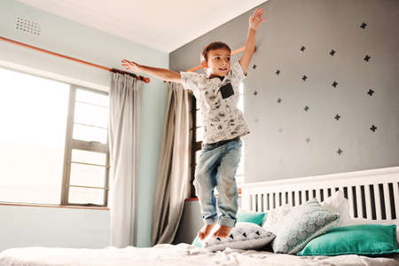 Full length shot of a cheerful young boy jumping on a bed in the bedroom at homeの写真素材