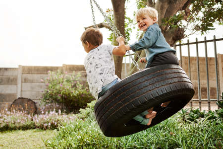 Shot of two adorable little boys playing on a swing together outdoorsの写真素材
