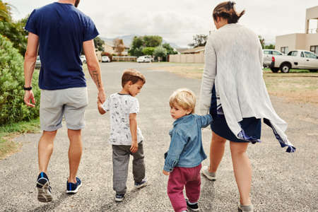Rearview shot of a young family holding hands and walking together in the neighbourhoodの写真素材