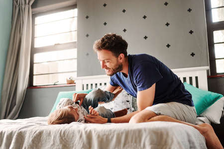 Shot of a cheerful young father and son playing together in the bedroom at homeの写真素材