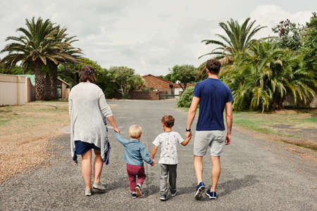 Rearview shot of a young family holding hands and walking together in the neighbourhoodの写真素材