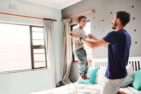 Shot of a cheerful young father and son playing together in the bedroom at homeの写真素材