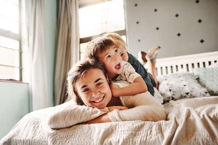 Portrait of a cheerful young mother playing with her little boys in the bedroom at homeの写真素材