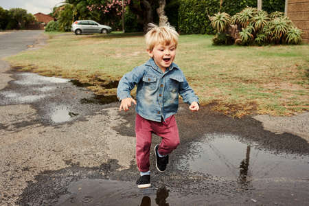 Shot of an adorable little boy playing in a puddle of water in the streetの写真素材