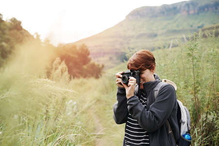 Shot of a young woman taking photos while out on a hike through the mountainsの写真素材