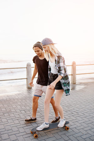 Full length shot of a handsome young man teaching his girlfriend how to skateboard on the promenade