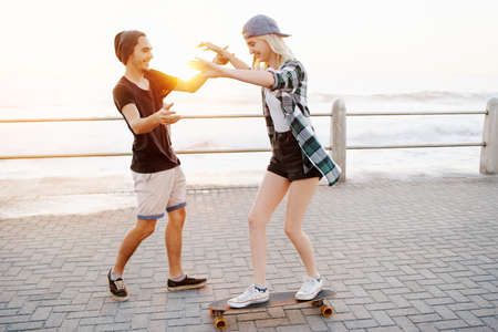 Full length shot of a handsome young man teaching his girlfriend how to skateboard on the promenadeの写真素材