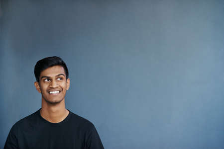 Studio shot of a cheerful young man smiling while being in deep thoughtの写真素材