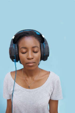 Shot of a cheerful young woman standing outside and listening to music on her phone with her eyes closedの写真素材