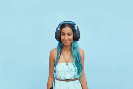 Shot of a cheerful young student listening to music with her headphones outside while looking at the cameraの写真素材