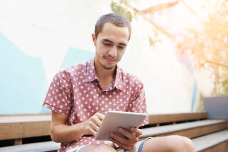 Shot of a young man sitting on the steps outside and using a digital tabletの写真素材
