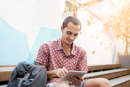 Shot of a young man sitting on the steps outside on campus and using a digital tabletの写真素材