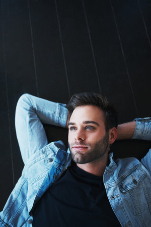 Shot of a handsome young man lying on the floor and looking pensiveの写真素材