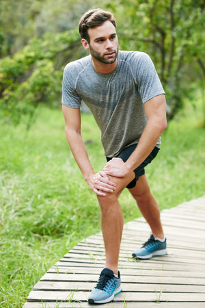 Shot of a young man stretching before his run in a park