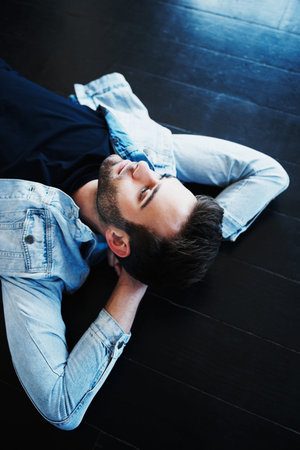 Shot of a handsome young man lying on the floor and looking pensive