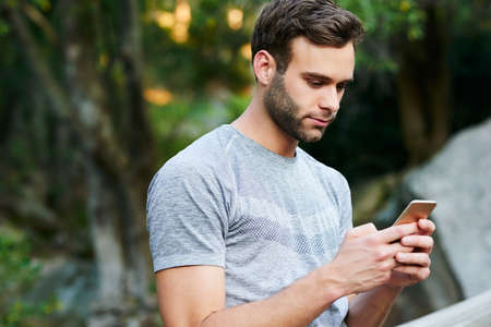 Cropped shot of a young man texting on his cellphone while out in a parkの写真素材