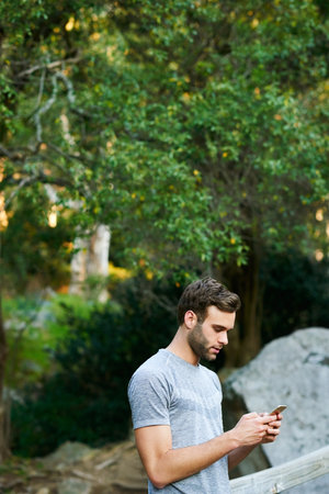 Cropped shot of a young man texting on his cellphone while out in a parkの写真素材