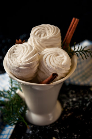 Homemade white marshmallows in white mug with cinnamon sticks on blackbackground. Winter timeの写真素材