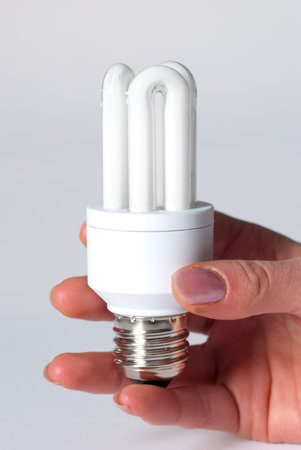 A hand holding a low energy lamp isolated against i white background