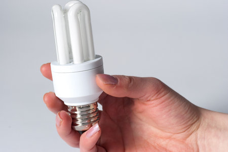 A hand holding a low energy lamp isolated against i white background