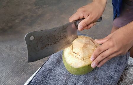 Two hand trying to open fresh coconuts with a large knife. coconut drink. の写真素材