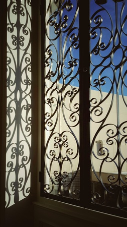 The sunlight hits the wrought iron window, creating a pattern on the wall.の写真素材