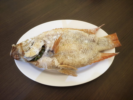 Salt-grilled ruby â€‹â€‹fish placed on a white plastic plate on a wooden table.It's a...
