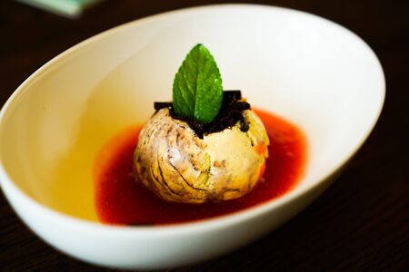 ice cream in white bowl with red sauce on wooden table with mint leafの写真素材
