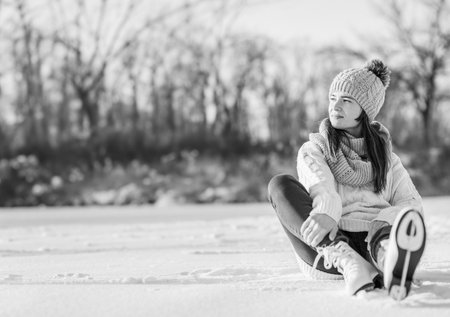 A young woman skates in a winter park. A girl in a warm sweater and hat sits on the ice and enjoys...