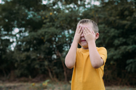 A boy plays hide and seek at home on the street. The child covers his eyes with his hands and counts. Blurry background and copy space for your advertising text message.の写真素材
