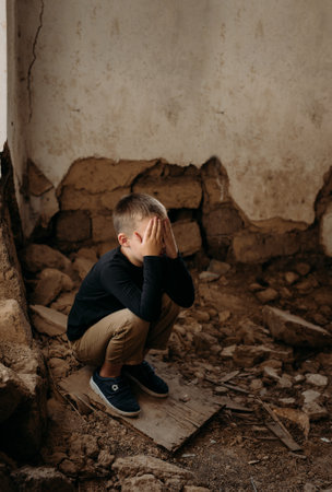A sad little Ukrainian child, a preschooler, sits on the ruins of his destroyed house after the arrival of a rocket in dark clothes and cries. War in Ukraine. Consequences of war.の写真素材