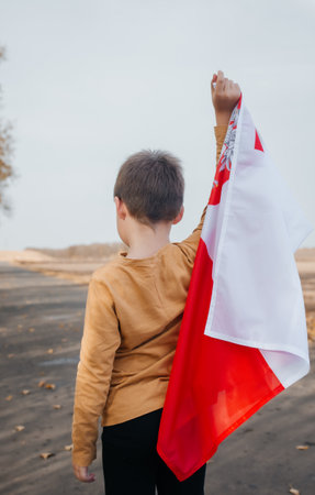 A little boy holds the flag of Poland in his hand. Portrait of a child with a national flag in nature. Rear view. Concept of national holidays and patriotic events. Patriotism. Independence Day.の写真素材
