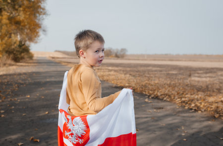 A handsome little boy behind his back holds the flag of Poland in his hands. Child standing on road with national flag on nature. Concept of national holidays and patriotic events. Independence Dayの写真素材