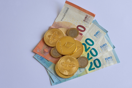 Pile of crypto currency coins over some Euro bills and coins isolated on a white backgroundの写真素材