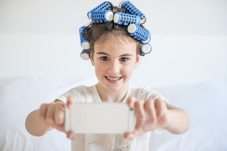 little girl posing with curlers and Smartphone, surprised and happyの写真素材